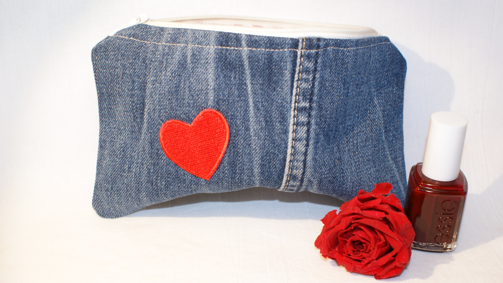 Jeansbeutel aus blauem Jeansstoff mit weißem Reißverschluss und die Vorderseite ziert ein rotes Herz .