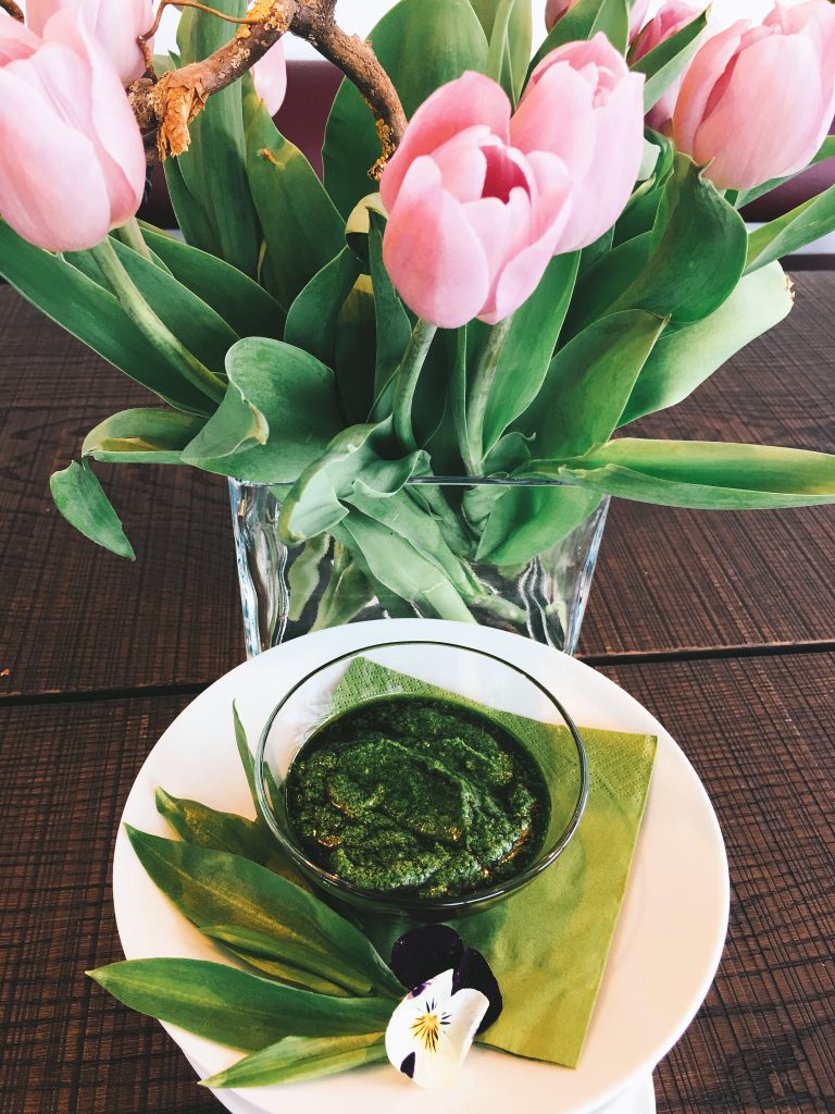 Bärlauchpesto in der Glasschale, daneben eine Vase mit Tulpen